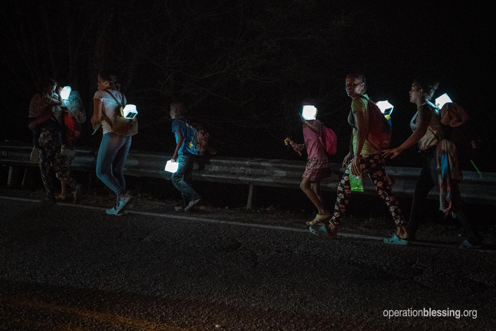 Venezuelan refugees walk on a highway in the dark with solar lamps from Operation Blessing.