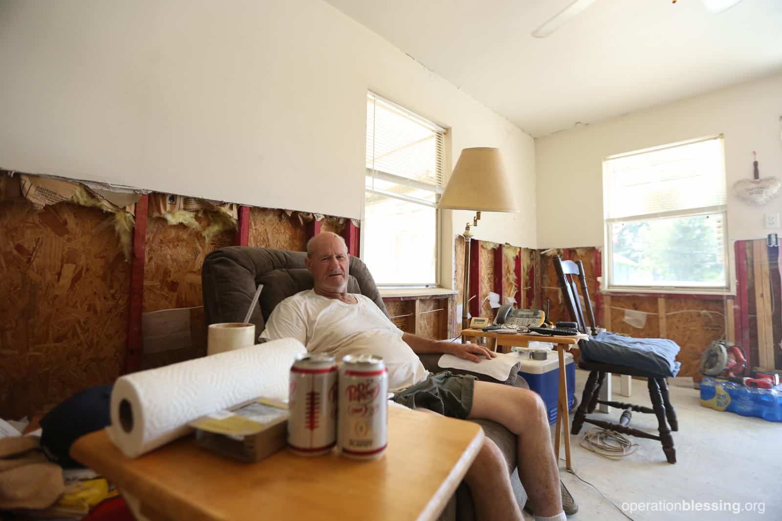 Allen sits in his stripped home on a single piece of furniture before the makeover.