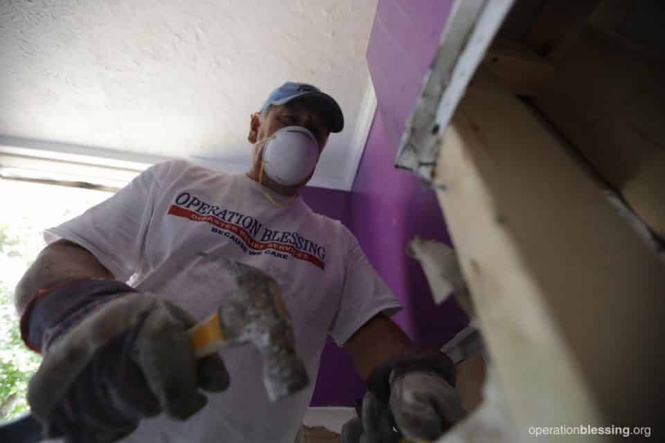 An Operation Blessing disaster relief volunteer helping with Divya's flooded home.