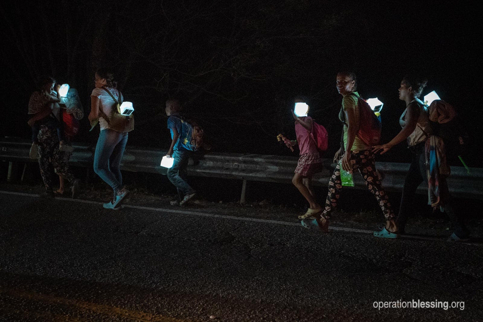 Venezuelan refugees walk on a highway in the dark with solar lamps from Operation Blessing.