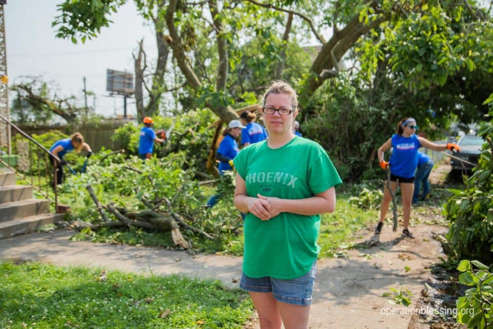 Nicole stands in her storm damaged yard as Operation Blessing volunteers provide tornado relief.